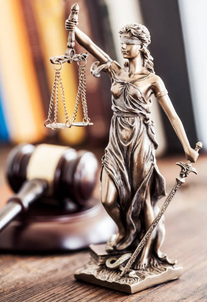 Bronze Lady Justice statue holding scales and sword with a judge's gavel blurred in the background.