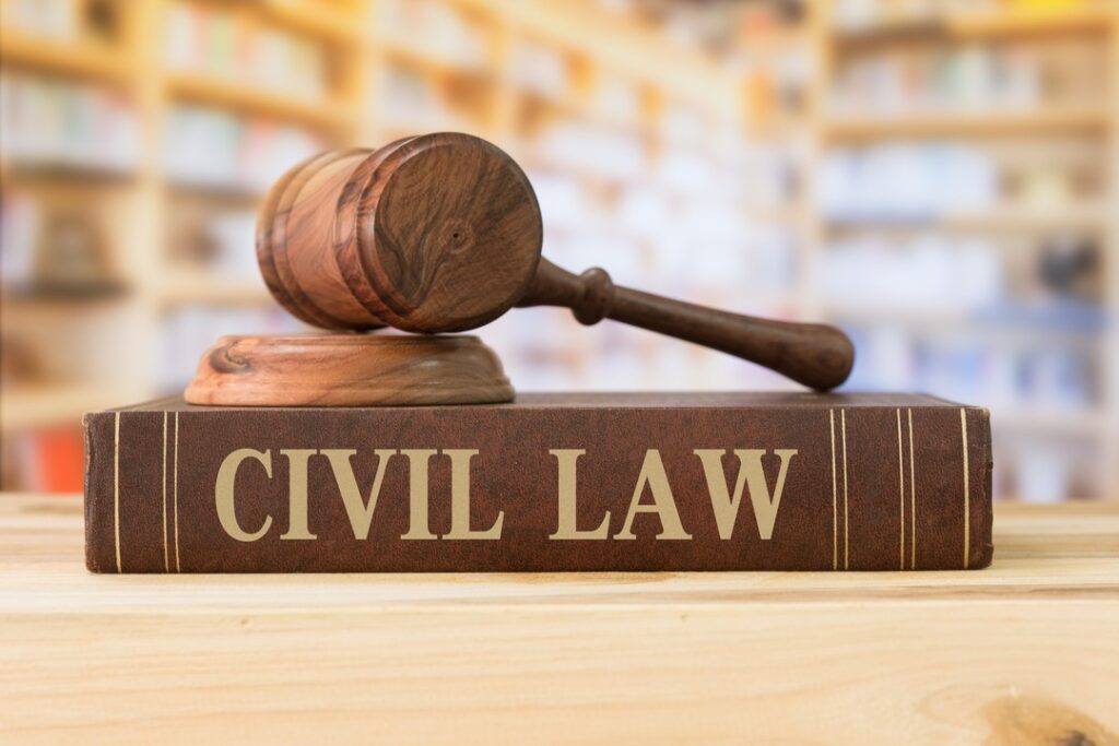 Wooden gavel resting on a large brown book titled "CIVIL LAW" in gold letters, with blurred bookshelves in the background.
